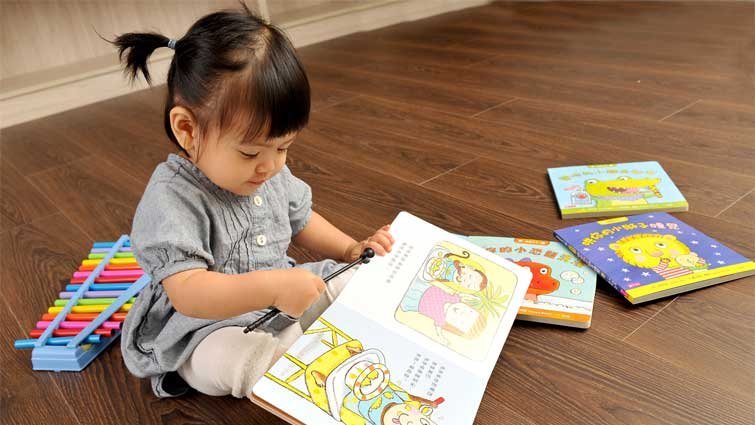 Bé 2 tuổi đang lật một cuốn sách tranh có hình các con vật ngộ nghĩnh, biểu cảm khuôn mặt thích thú khi nhận ra con chó và con mèo quen thuộc.